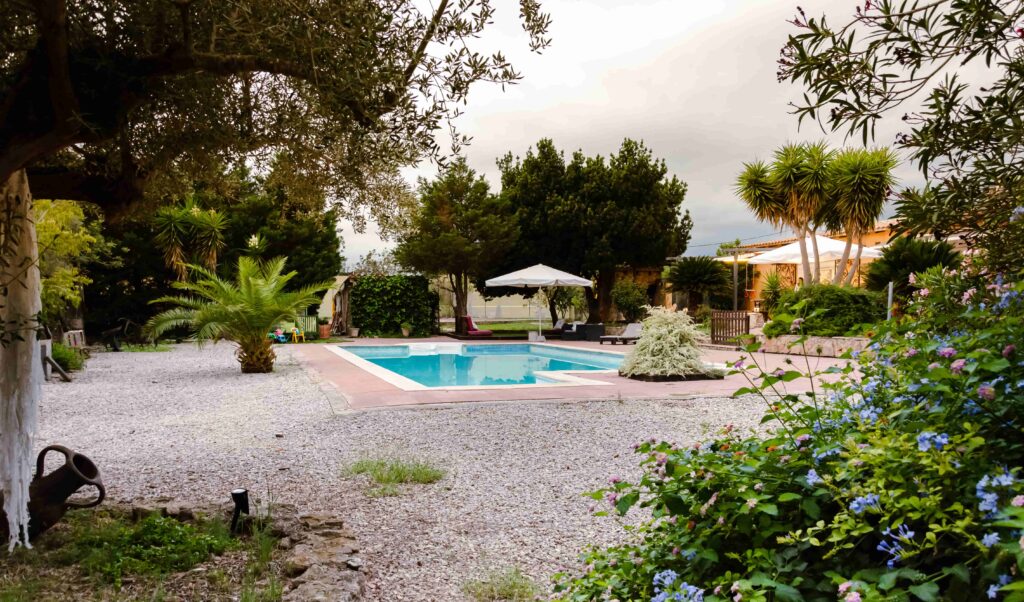 Rústica vista de piscina enmarcada por jardín frondoso y camino de grava