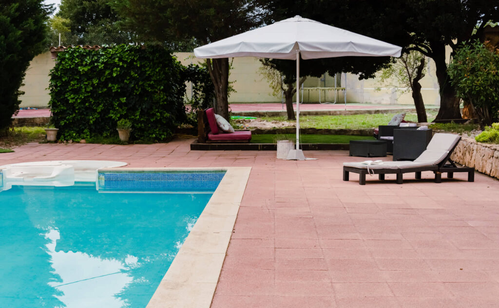 Amplia zona de piscina al aire libre con sombrilla y tumbonas